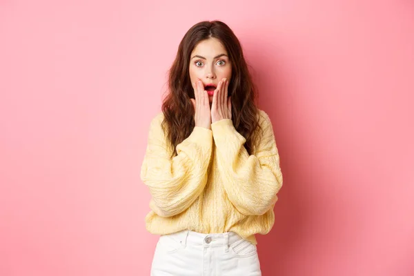 Immagine di donna bruna scioccata e sorpresa che ansima, controlla grandi notizie, bocca aperta, tenendosi per mano sul viso, in piedi stupito sullo sfondo rosa — Foto Stock