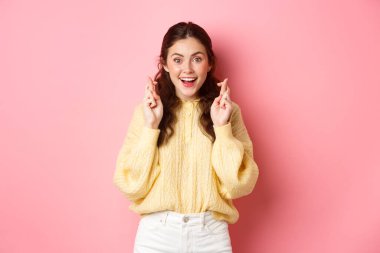 Şanslı şirin kız şans diliyor ve gülümsüyor, hayaller gerçek oluyor, dilek tutuyor, sınav sonuçlarını bekliyor ve pembe arka planda umut dolu görünüyor.