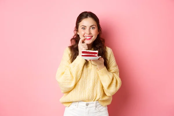 Imagem da menina animado pensando em comer bolo delicioso, mordendo o dedo da tentação e olhando atencioso para a câmera, pense em calorias na sobremesa, fundo rosa — Fotografia de Stock