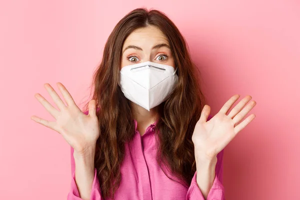 コロナウイルス,予防措置と健康の概念.驚きと興奮した女性のポートレートを閉じますマスク,手を上げと息をのむような,ピンクの背景 — ストック写真