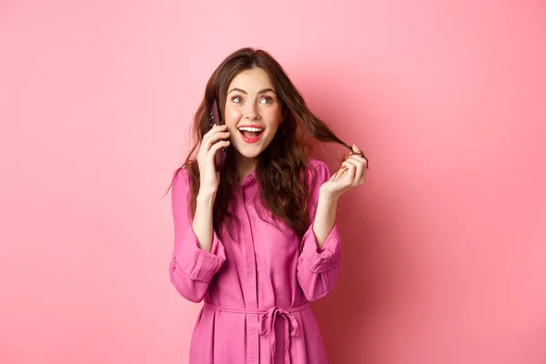 Glamour garota falante brincando com o cabelo, fazendo a ordem, chamando alguém no telefone, falando no smartphone, de pé contra fundo rosa — Fotografia de Stock
