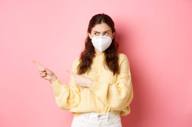 Covid, Corona ve sosyalleşme konsepti. Tıbbi solunum cihazındaki kafası karışmış esmer kızın şüpheleri var, sol fotokopi alanını işaret ediyor ve ona bakıyor, pembe arka planda duruyor.