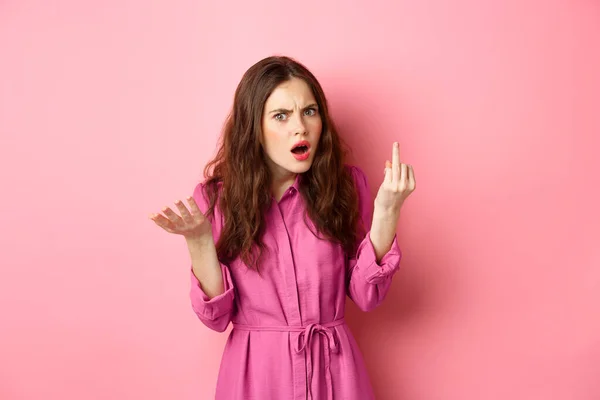 Ragazza infastidita litigando sulla proposta, vuole sposarsi, mostrando il dito senza anello di fidanzamento, in piedi confuso sullo sfondo rosa — Foto Stock