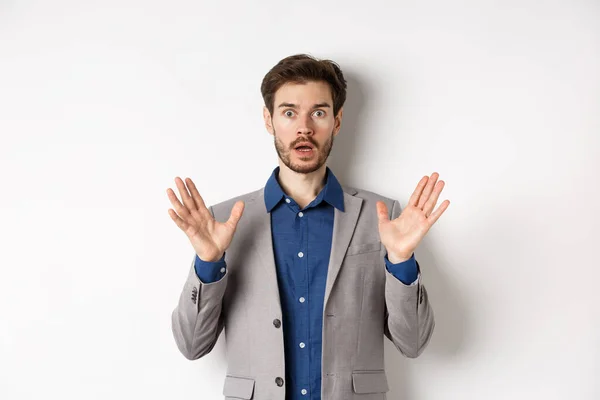 Empresário surpreso em terno levantando as mãos para cima e olhar animado, de pé contra fundo branco — Fotografia de Stock
