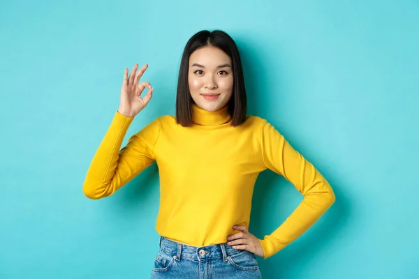 Belle femme asiatique souriante recommander le produit, montrant Ok signe et regardant satisfait, debout sur fond bleu — Photo