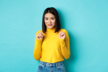 Mide bulandırıcı, tiksindirici, asık suratlı, mavi arka planda duran iğrenç bir şeyden geri adım atan Çinli bir kadın tasviri.