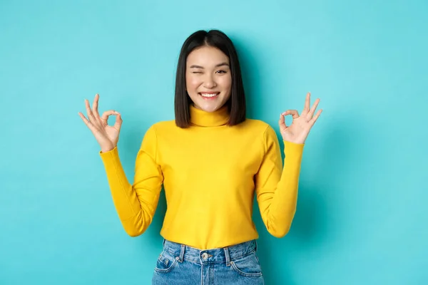 Modèle féminin asiatique joyeux montrant des gestes corrects, souriant et regardant impressionné, produit de louange, debout sur fond bleu — Photo