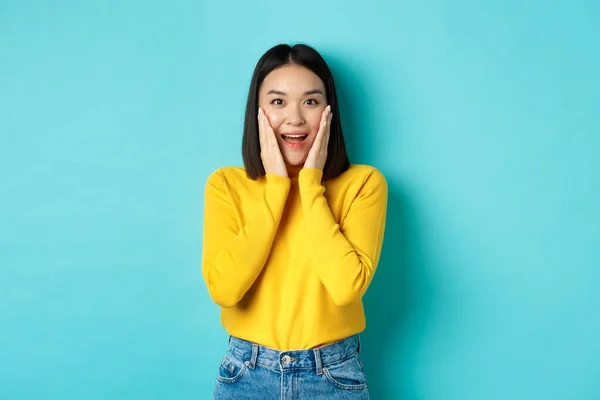 Image de femme asiatique joyeuse et surprise vérifiant la promotion, haletant étonné, debout sur fond bleu — Photo