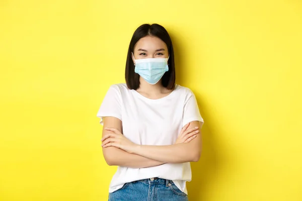 Covid, sjukvård och pandemi koncept. Asiatisk kvinna i vit t-shirt och medicinsk mask kors armar på bröstet och tittar på kameran — Stockfoto