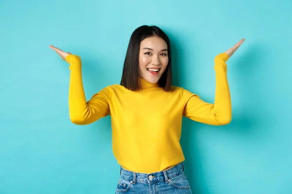 Concept beauté et mode. élégant belle asiatique fille démontrer promotion levant les mains vers le haut et souriant, montrant quelque chose sur fond bleu — Photo