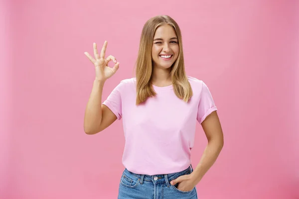 Podes contar comigo. Retrato de confiante e assertiva jovem assistente de loja feminina garantindo produto é grande sorrindo amplamente piscando para a câmera e mostrando gesto ok em como e aprovação — Fotografia de Stock