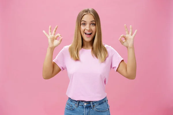 Portret pełnej entuzjazmu, atrakcyjnej białej dziewczyny w modnej koszulce i dżinsach prezentujących się dobrze lub potwierdzających gest z rozbawionym szerokim uśmiechem stojącym zadowolonym z różowego tła reagującym na znakomite wiadomości — Zdjęcie stockowe