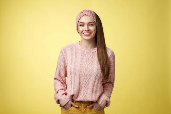 Γοητευτικό φιλικό νεαρό κορίτσι σε πλεκτό πουλόβερ και κορδέλα κρατώντας τα χέρια στις τσέπες, χαμογελώντας, αναζητούν θετικά κίνητρα επίτευξη των στόχων που έχουν μεγάλη μέρα, θέτοντας θετικά σε κίτρινο φόντο — Φωτογραφία Αρχείου