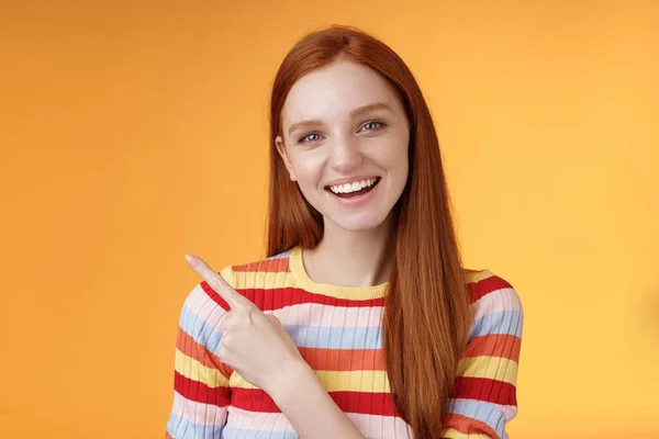 Vriendelijk uitgaande goed uitziende gember meisje student bespreken college klasgenoot glimlachen wijzend linksboven ondervraagd nieuwsgierig weten details staande oranje achtergrond — Stockfoto