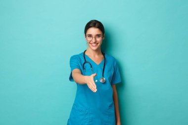 Coronavirus, salgın hastalık ve sosyalleşme konsepti. Kendine güvenen güzel bir kadın doktor resmi, el sıkışmak için gülümseyen ve uzanan bir el, hastayı selamlayan, mavi arka planda duran