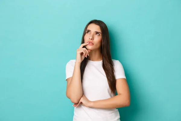 Afbeelding van bedachtzame mooie vrouw in wit t-shirt, opkijken en denken, keuze maken, over blauwe achtergrond staan en nadenken — Stockfoto