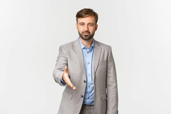 Retrato de empresário confiante com barba, vestindo terno cinza, estendendo a mão para aperto de mão, cumprimentando você, apresentar-se, em pé sobre fundo branco — Fotografia de Stock