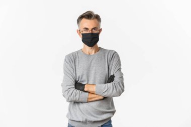 Koronavirüs, yaşam tarzı ve karantina kavramı. Sağlık maskeli ve eldivenli orta yaşlı bir adamın portresi göğsünde çapraz kollar ve beyaz arka planda duran hayal kırıklığına uğramış gibi görünüyor.