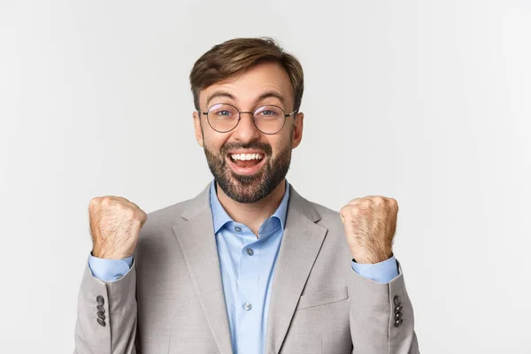 Close-up of successful businessman in glasses and gray suit, rejoicing, saying yes with happy face and making fist pump, achieve goal, standing over white background — Stock Photo, Image