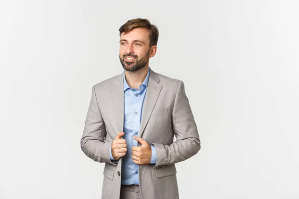 Imagem de empresário bem sucedido e confiante em terno cinza e camisa azul, sorrindo satisfeito e olhando para a esquerda, em pé sobre fundo branco — Fotografia de Stock