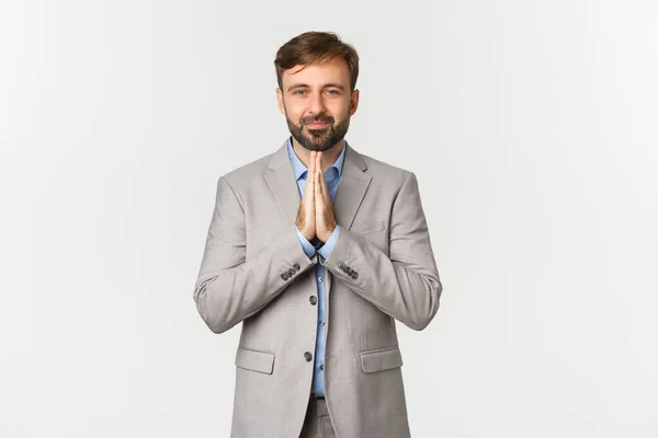 Portrait of handsome bearded man in grey suit, thanking for something, begging for help, smiling hopeful, standing over white background — Stock Photo, Image