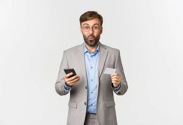 Portrait d'un homme d'affaires excité tenant carte de crédit et téléphone mobile, faisant des achats et payant en ligne, debout sur fond blanc — Photo