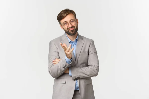 Portrait of doubtful businessman with beard, wearing glasses and suit, grimacing and looking skeptical, standing indecisive over white background — Stock Photo, Image
