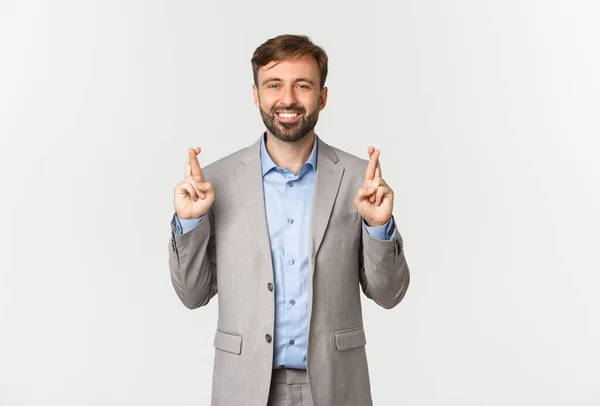 Retrato de bem sucedido sorridente empresário fazendo desejo, cruzando os dedos para a boa sorte, à espera de resultados, de pé sobre fundo branco — Fotografia de Stock
