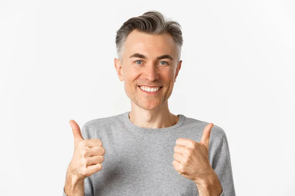 Close-up de homem de meia-idade alegre, sorrindo feliz e satisfeito, mostrando polegar-se, expressando aprovação, como algo bom, de pé sobre fundo branco — Fotografia de Stock