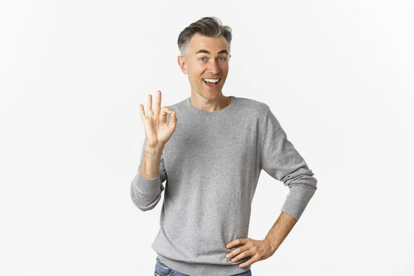 Image of handsome and cheerful middle-aged man showing support, make okay sign and smiling satisfied, approve and agree, saying yes, standing over white background — Stock Photo, Image