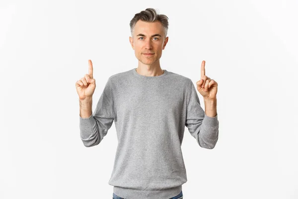 Porträt eines gutaussehenden Mannes mittleren Alters in grauem Pullover, der Promo zeigt, mit erhobenem Finger ernst guckt und vor weißem Hintergrund steht — Stockfoto