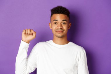 Yakışıklı, gülümseyen, umutlu ve yumruğunu kaldıran Afro-Amerikan erkeğinin yakın çekimi. Siyahların hayatlarının işaretini gösteriyor. Haklar için savaşıyor, mor arka planda duruyor.