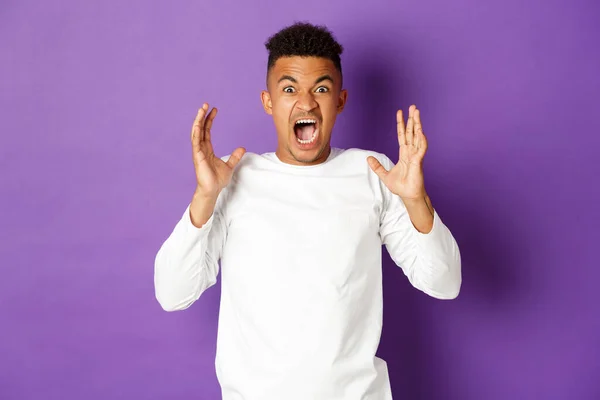 Imagen de hombre afro-americano frustrado, gritando y mirando enojado, perdiendo los estribos de la ira, de pie angustiado contra el fondo púrpura —  Fotos de Stock