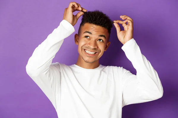 Obrázek veselého mladého afroameričana, jak se dotýká jeho vlasů a usmívá se, stojí nad purpurovým pozadím — Stock fotografie