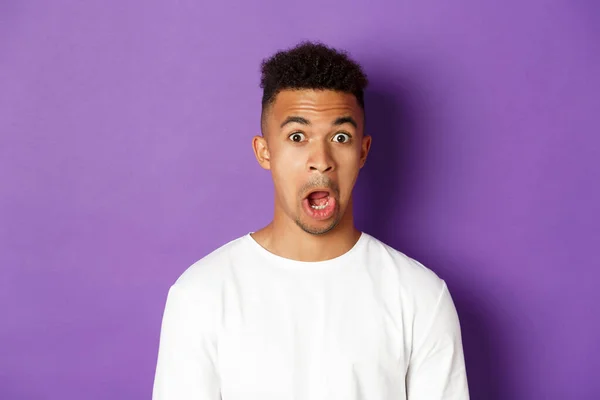 Close-up de impressionado homem afro-americano, mandíbula cair e olhar para algo espantado, de pé sobre fundo roxo — Fotografia de Stock