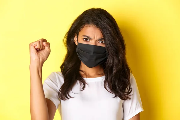 Concepto de covidio-19, distanciamiento social y estilo de vida. Primer plano de la feroz y confiada mujer afroamericana, siendo una manifestante en movimiento de la materia de vidas negras, mostrando un puño, usando mascarilla facial — Foto de Stock