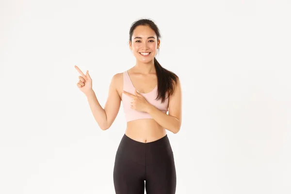 Esporte, bem-estar e conceito de estilo de vida ativo. Sorrindo magro e bonito asiático fitness girl, atleta feminino apontando dedos canto superior esquerdo, mostrando equipamento de treino venda promo ou oferta de ginásio — Fotografia de Stock