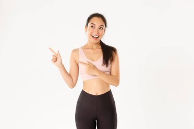 Spor, refah ve aktif yaşam tarzı konsepti. Heyecanlı, ince ve tatlı Asyalı fitness kızı, sol üst köşeyi gösteren bayan sporcu, spor malzemeleri satış promosyonu veya spor salonu teklifi gösteriyor..