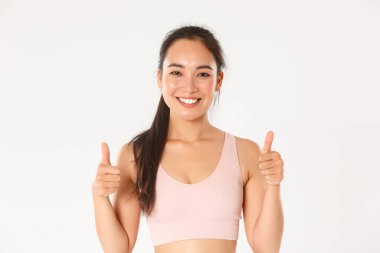 Spor, refah ve aktif yaşam tarzı konsepti. Mutlu şirin esmer Asyalı kız, fitness eğitmeni tatmin olmuş görünüyor, baş parmağını kaldırıyor ve gülümsüyor, iyi bir egzersiz yapıyor.