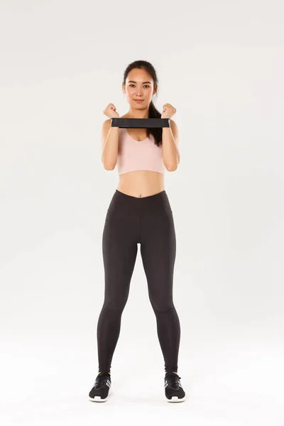 Full längd av leende och beslutsam, smal brunett asiatisk fitness flicka, träningscoach visar övningar med motstånd stretching rep, tittar på kameran, demonstrera träningsutrustning — Stockfoto