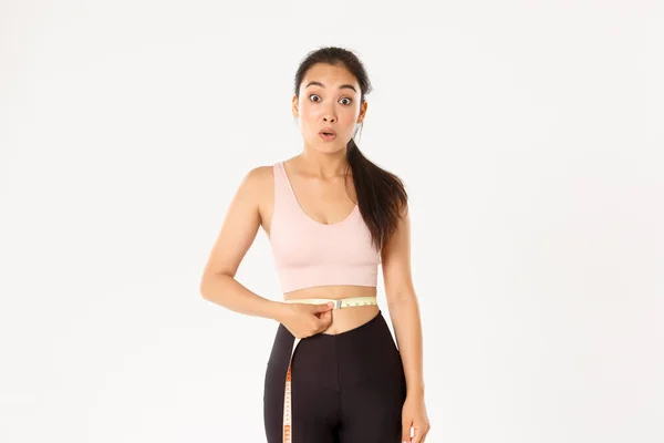 Озил, концепция здорового образа жизни и благополучия. Удивленный азиатская девушка на диете, спортсменка обертывания измерительной лентой вокруг талии и выглядеть впечатлен, как похудеть с тренировкой — стоковое фото