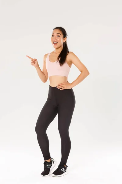 Deporte, gimnasio y concepto corporal saludable. Longitud completa de excitado asiático mujer atleta en sportsbra y leggings apuntando y mirando esquina superior izquierda emocionado, encontrado buenos precios para gimnasio equipo — Foto de Stock