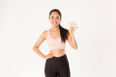 Spor, refah ve aktif yaşam tarzı konsepti. Gülümseyen tatlı esmer Asyalı sporcu, dört parmak gösteren fitness kızı, mükemmel vücut için temel kuralları açıkla, en iyi egzersizler, beyaz arka plan