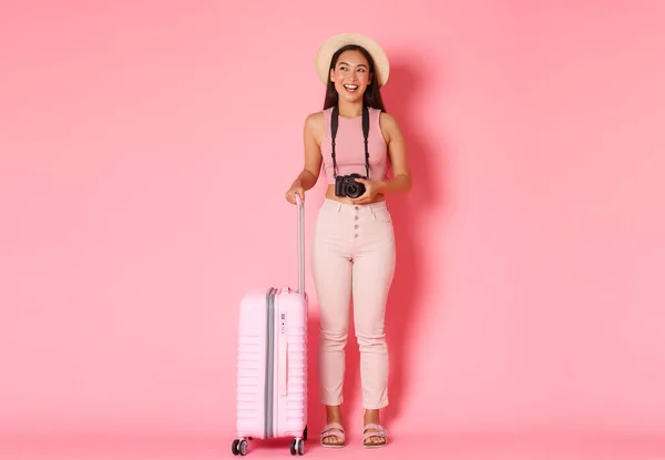 Tourismus, Sommerurlaub, Urlaub im Ausland. Volle Länge des glücklichen attraktiven asiatischen Mädchen Touristin, Reisende in Strohhut mit Kamera und Koffer lachen und lächeln, rosa Hintergrund — Stockfoto