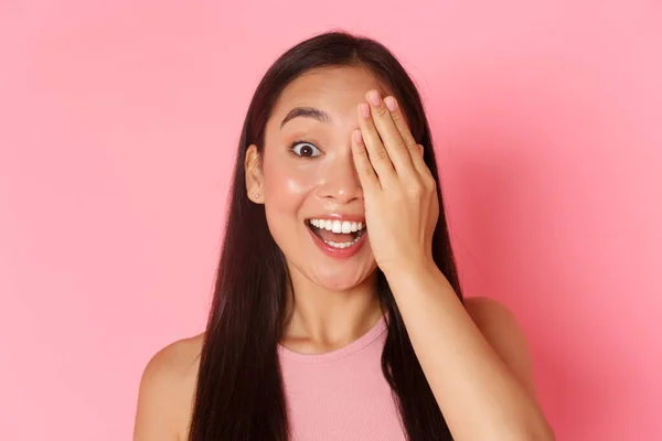 Concepto de belleza, moda y estilo de vida. Retrato de alegre sonrisa chica asiática cubrir la mitad de la cara para mostrar antes y después o comprobar la vista en óptico, de pie sorprendido sobre fondo rosa — Foto de Stock