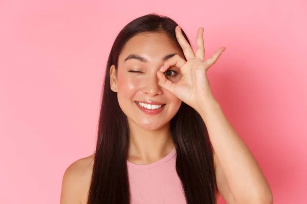 Beauté, mode et style de vie concept. Portrait de kawaii attrayant asiatique fille montrant un bon geste sur les yeux et clin d'oeil insouciant à la caméra, souriant heureux, garantir la qualité, recommander endroit — Photo