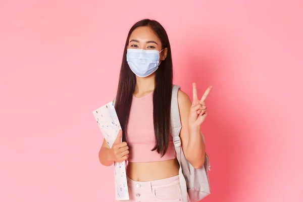 Safe tourism, travelling during coronavirus pandemic and preventing virus concept. Happy asian girl travel in pandemic covid-19 with medical mask, holding map, show peace sign, tourist going abroad — Stock Photo, Image