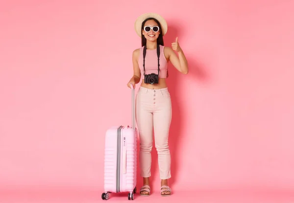 Туризм, літні канікули, канікули за кордоном концепція. Повна довжина красивих розслаблених азіатських туристів, мандрівників в сонцезахисних окулярах і літньому одязі показують великі пальці вгору, як готель, рожевий фон — стокове фото