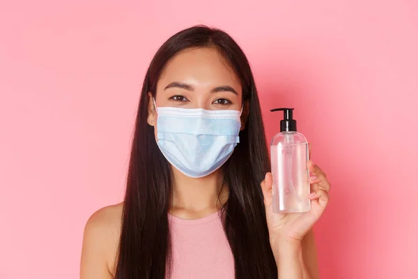 Covid-19 salgını, koronavirüs ve sosyal uzaklık kavramı. Neşeli Asyalı kızın sadece tıbbi maskeyle alışverişe çıkması ve el dezenfektanı ile önleyici önlemler alınmasını öneriyor. — Stok fotoğraf