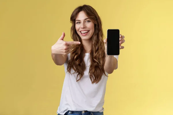 Fröhlich frech gut aussehende gesellige Mädchen lockiges langes Haar verlängerter Arm Smartphone Zeigefinger Handybildschirm breit lächelnd empfehlen coole App-Blogger fördern soziale Seite — Stockfoto